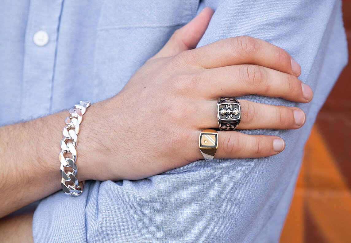 Do Men Wear Promise Rings? Two mens rings on a hand with a chain bracelet.