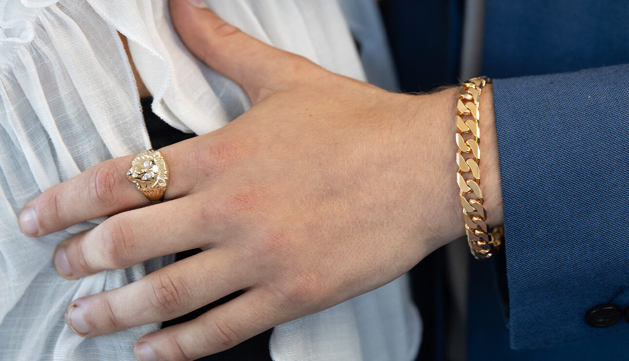 a mens hand wearing a gold ring and a bracelet