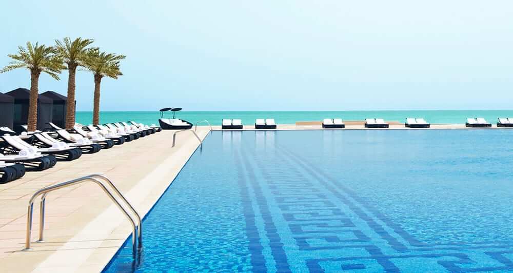 Hotel pool with loungers and the Arabian Gulf in the bakground