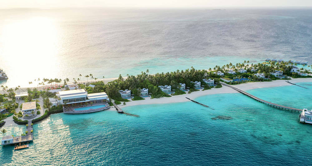 Jumeirah Maldives at Olhahali Island with the modern chic beach villas visible across the island, with the turquoise Maldives lagoon in front of them.