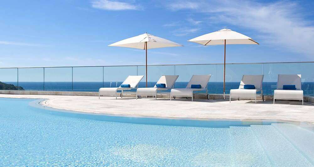 The rooftop pool at Jumeirah Port Soller Hotel & Spa, Mallorca with white loungers and beach umbrellas. The Balearic Sea is visible in the background.