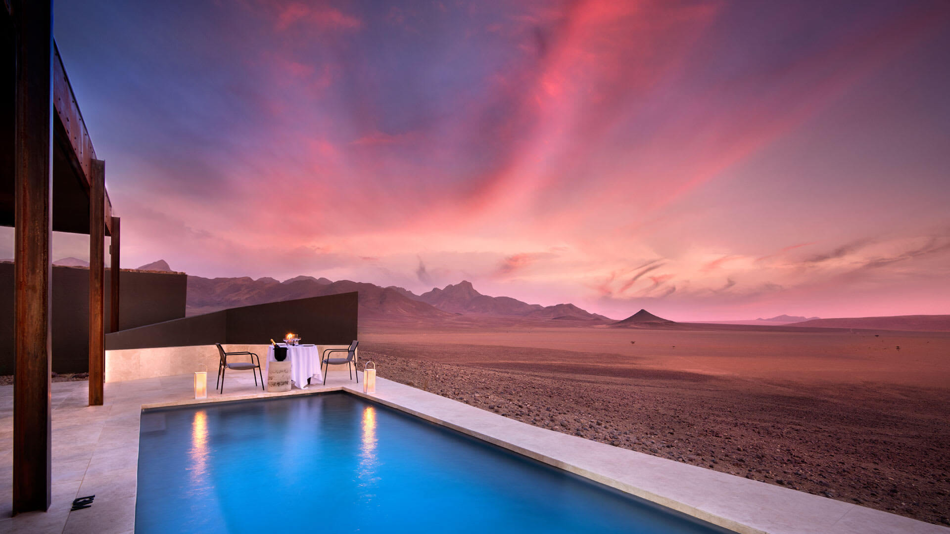 Swimming pool with te desert in the background as the sunsets with a pink sky