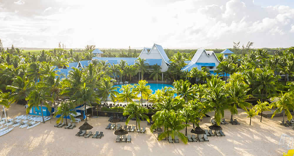 Palm trees encircle the pool of  Victoria Beachcomber Resort & Spa, with a soft sandy beach and loungers in front.